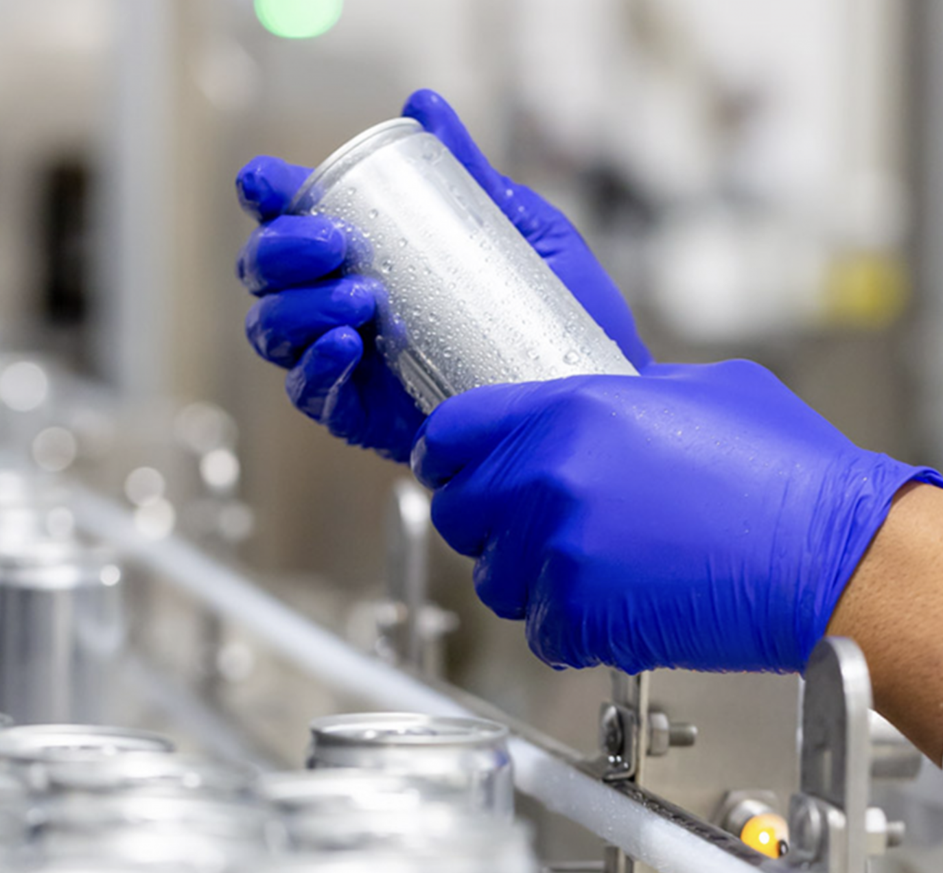Gloved Peak production worker checking a finished can on the beverage line